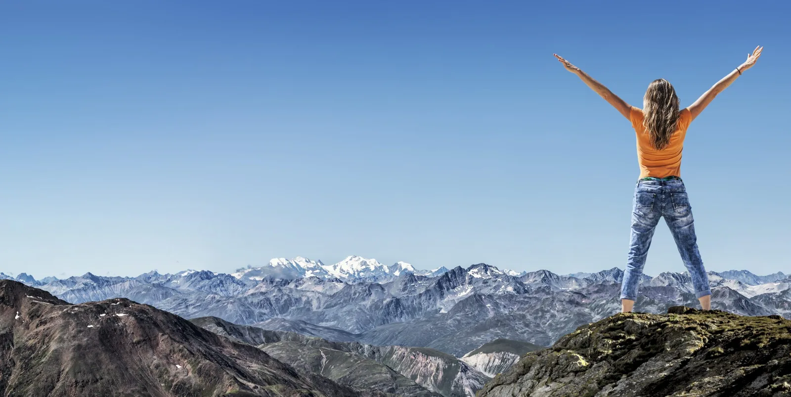 Frau mit ausgestreckten Armen auf einem Berggipfel vor einem Alpenpanorama